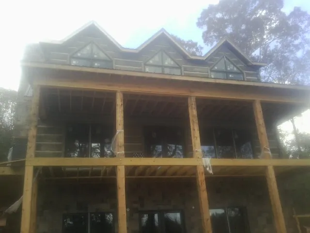 Dormers and porch framing on a large log home under construction — Roof Coating work by our crew in Lenox